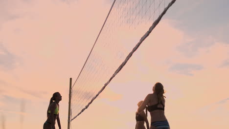 SLOW-MOTION-LOW-ANGLE-CLOSE-UP-SUN-FLARE:-Athletic-girl-playing-beach-volleyball-jumps-in-the-air-and-strikes-the-ball-over-the-net-on-a-beautiful-summer-evening.-Caucasian-woman-score-a-point.